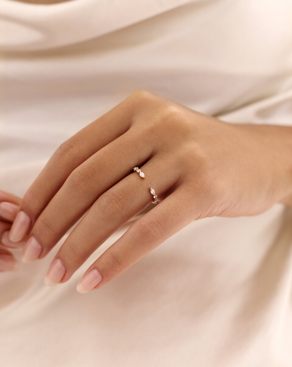 Close-up of a hand wearing the Marquise + Round Open Diamond Band in 14k rose gold, featuring marquise and round natural diamonds against ivory satin. 14k Yellow Gold 14k White Gold 14k Rose Gold Platinum 