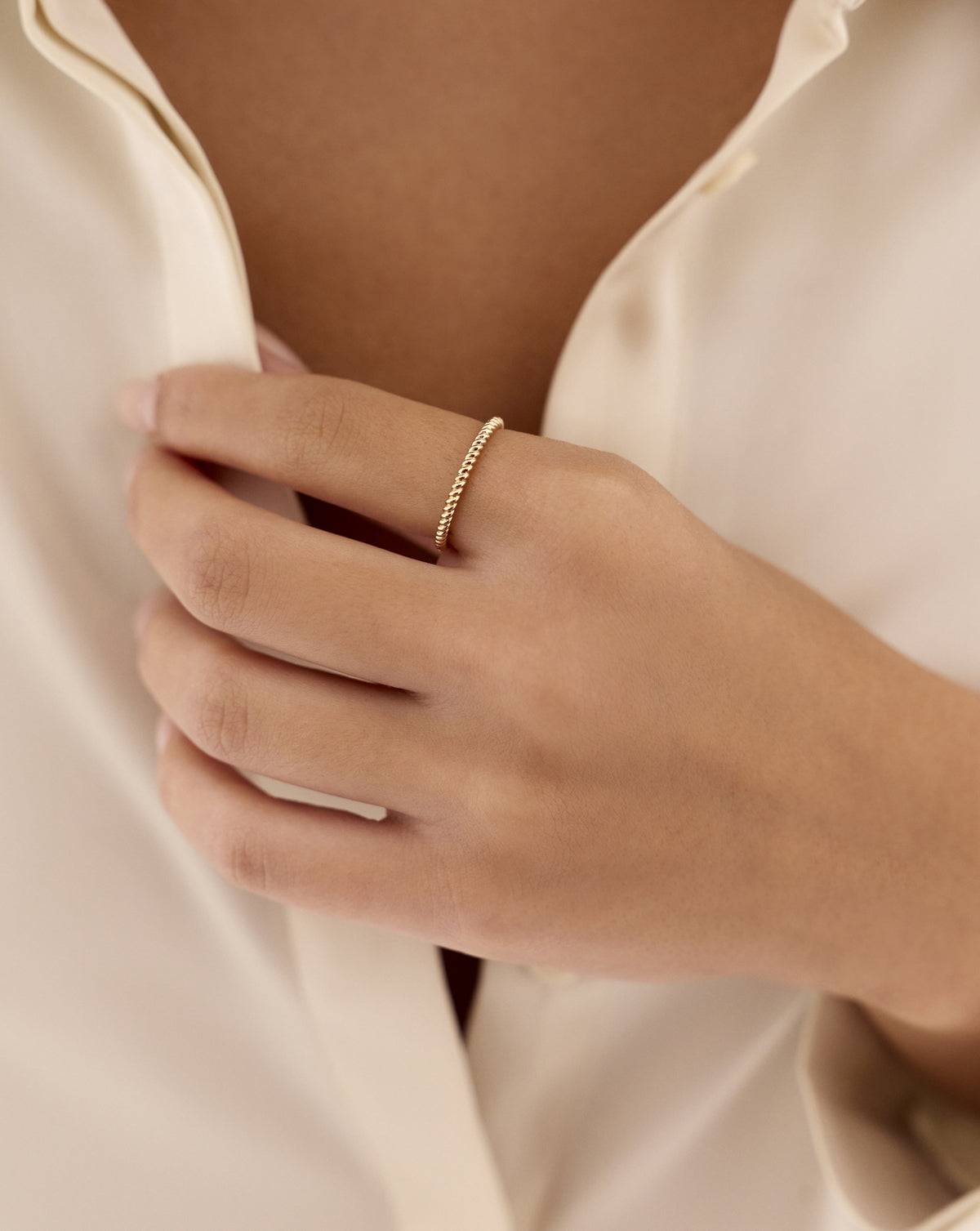 Close-up of a hand wearing the 14k yellow gold Classic Twisted Ring, featuring a slim, rope-inspired twisted band while gently holding an ivory blouse. 14k yellow gold sterling silver