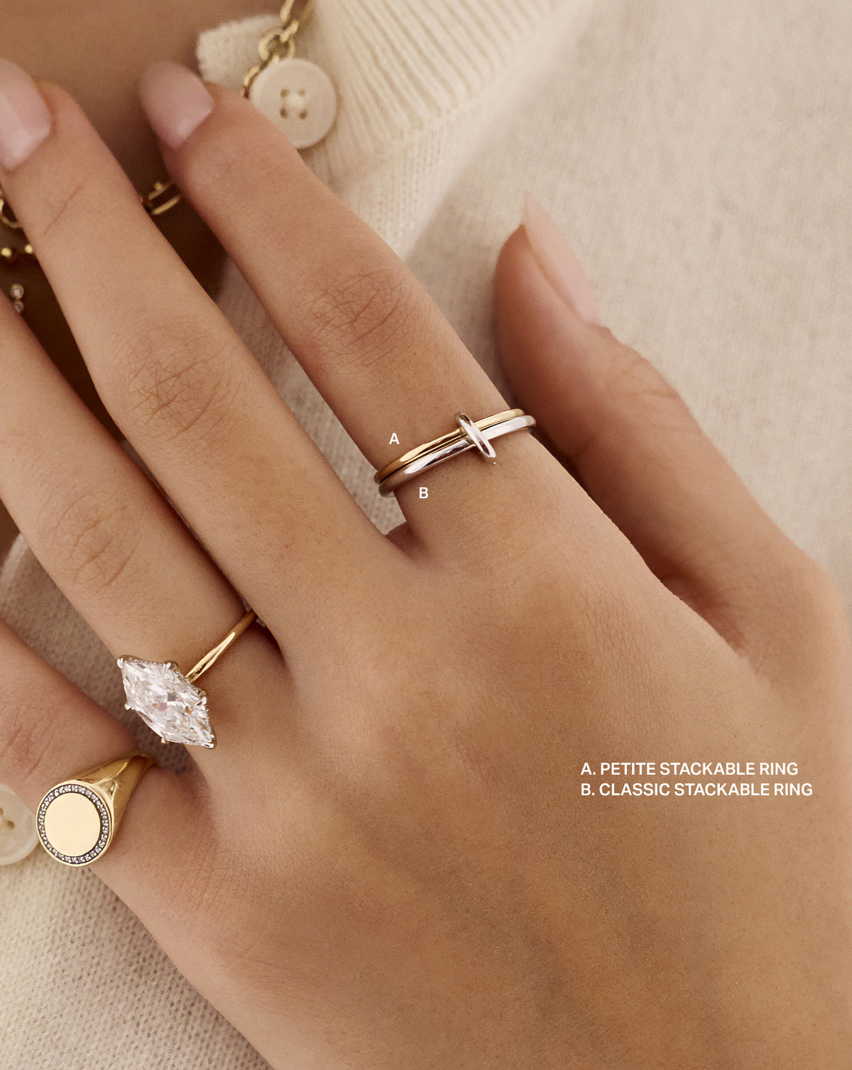 Close-up of a hand wearing the Petite Stackable Ring (A) and Classic Stackable Ring (B), linked by an oval clasp and styled with marquise diamond and round signet rings. 14k yellow gold Sterling Silver