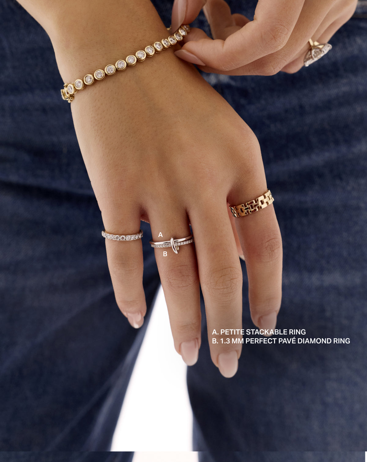 Close-up of a hand wearing the Petite Stackable Ring (A) and 1.3 mm Perfect Pavé Diamond Ring (B), linked by the ring clique clasp against dark blue denim. 14k yellow gold Sterling Silver 