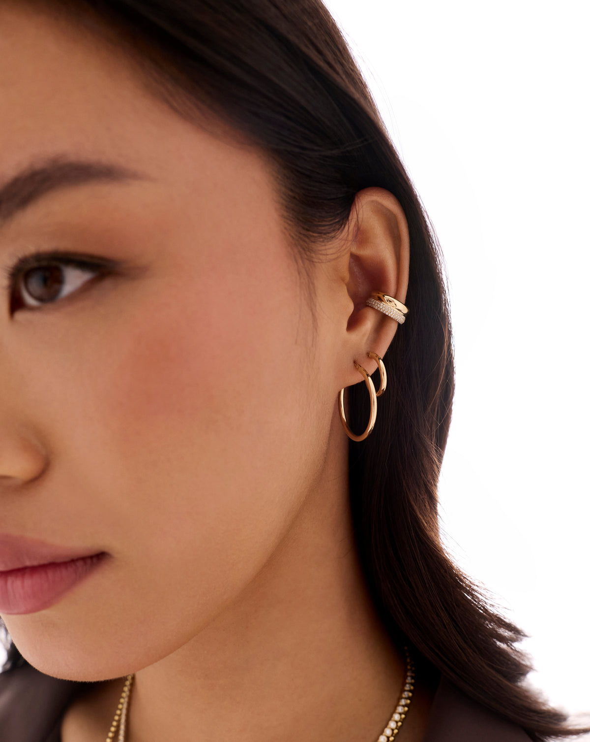 Gold double-row pavé ear cuff with sparkling clear stones worn on the upper ear, paired with a gold hoop earring.