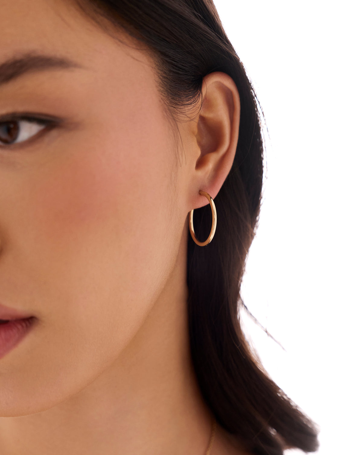 global essential medium hoop earring worn on the ear, shown in a close-up side profile against a white background.