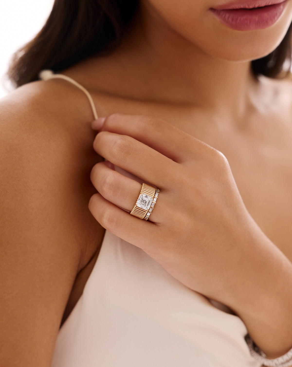 Model holding an ivory dress strap while wearing the Ribbon ring with a 2.85-carat Asscher-cut lab-grown diamond on a wide, fluted yellow gold band, stacked with a slim diamond band.