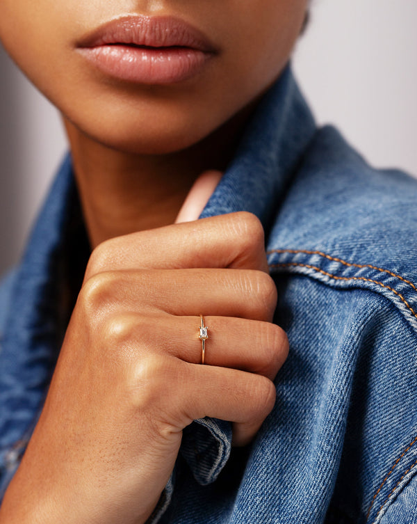 Single Emerald Diamond Ring worn on ring finger of hand holding collar of denim jacket