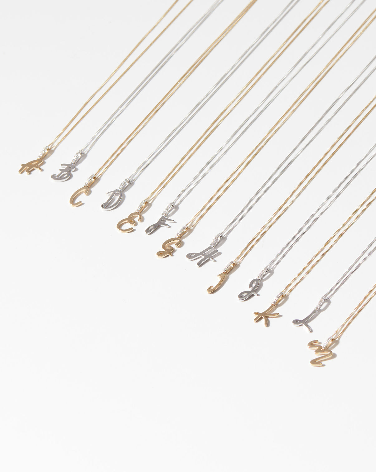 Script Initial Necklaces in a flat lay with letters A-M in yellow gold and white gold