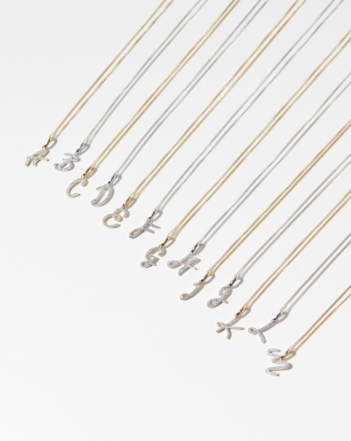 Diamond Script Initial Necklaces in a flat lay with letters A-M in yellow gold and white gold