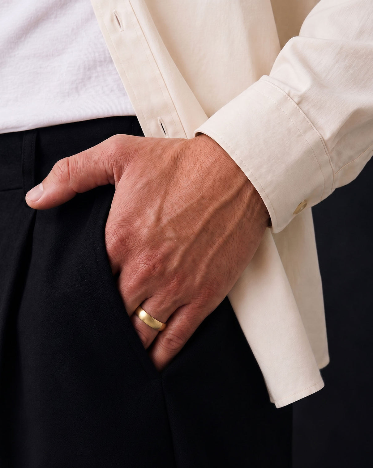 A close-up of a man's hands resting in his pocket, wearing a simple gold band ring on his left ring finger.  global