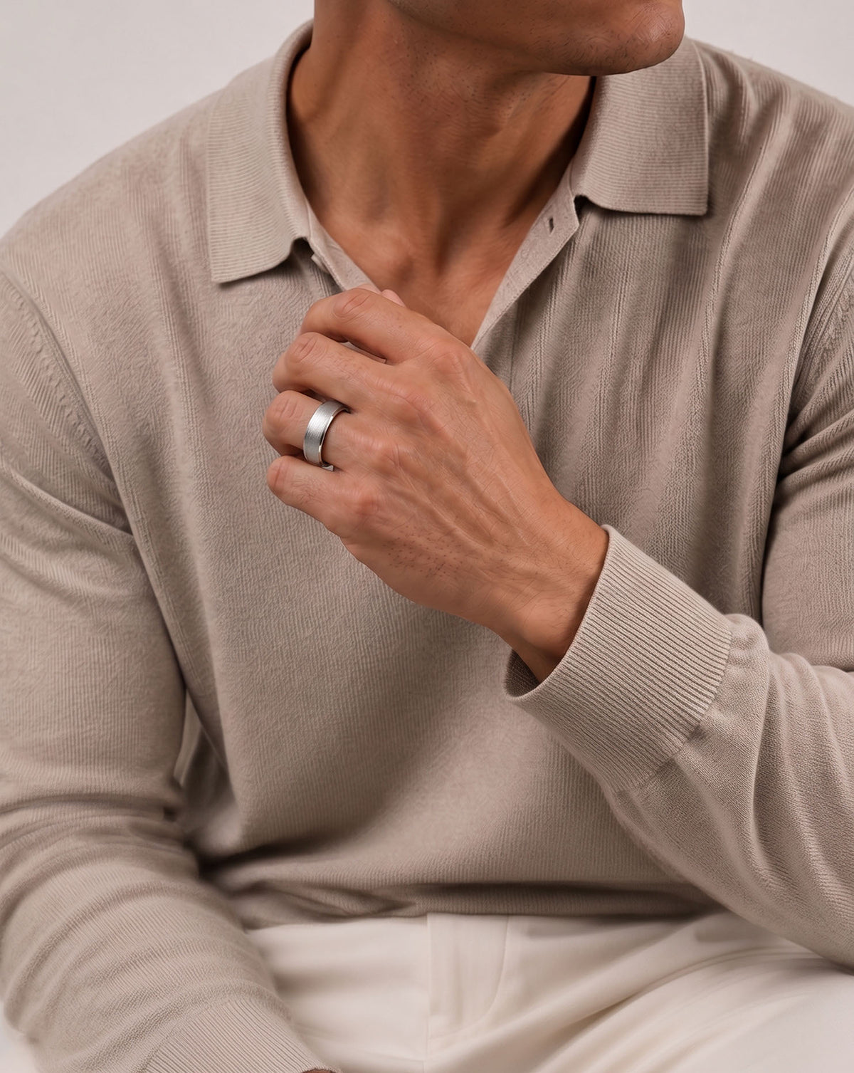 A close-up of a man's hands trying to fix his collar, wearing a simple white gold band ring on his left ring finger.  global