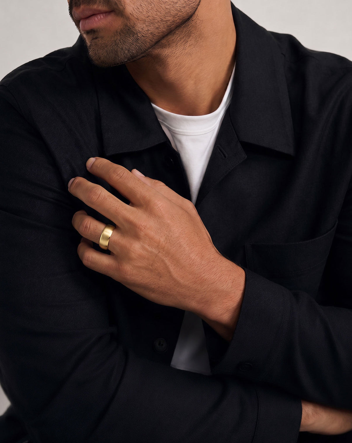 A close-up of a man's hands fixing his collar, wearing a simple gold band ring on his left ring finger.  global