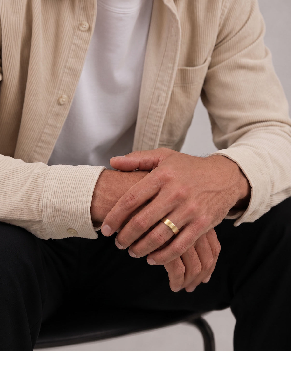 A close-up of a man's hands resting on his lap, wearing a simple gold band ring on his left ring finger.  global