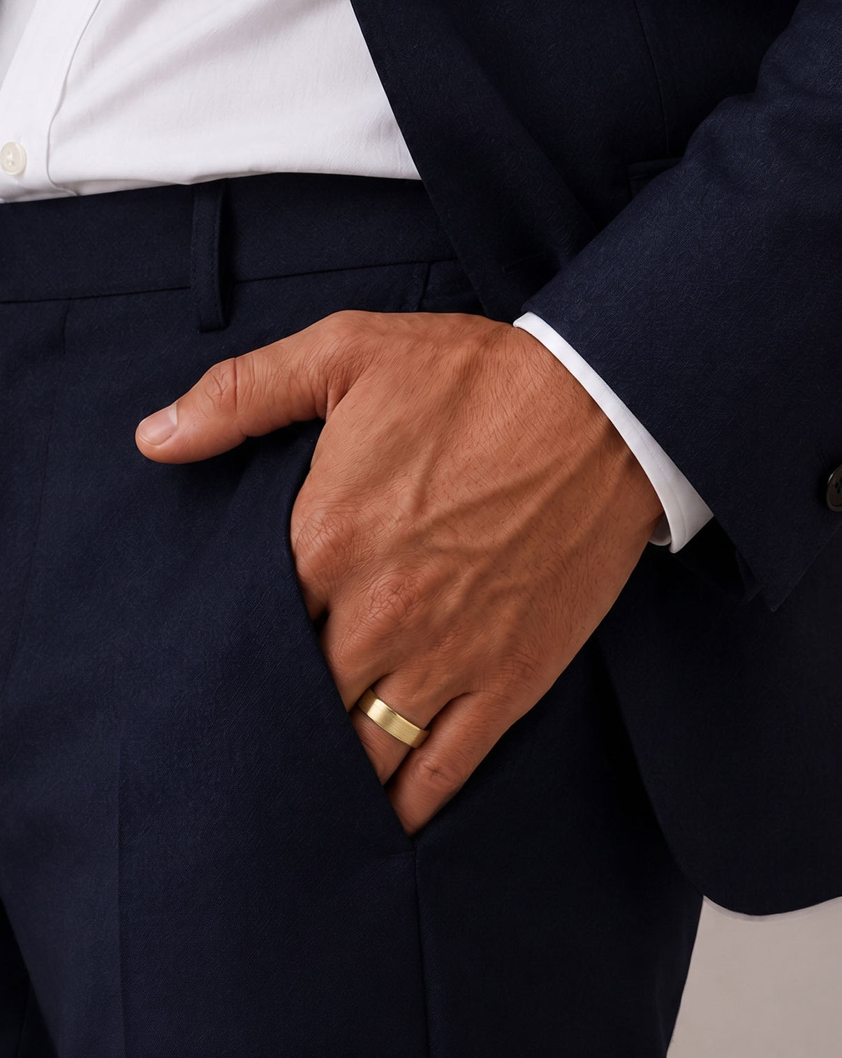 A close-up of a man's hand inside his pocket, wearing a simple gold band ring on his left ring finger.  global