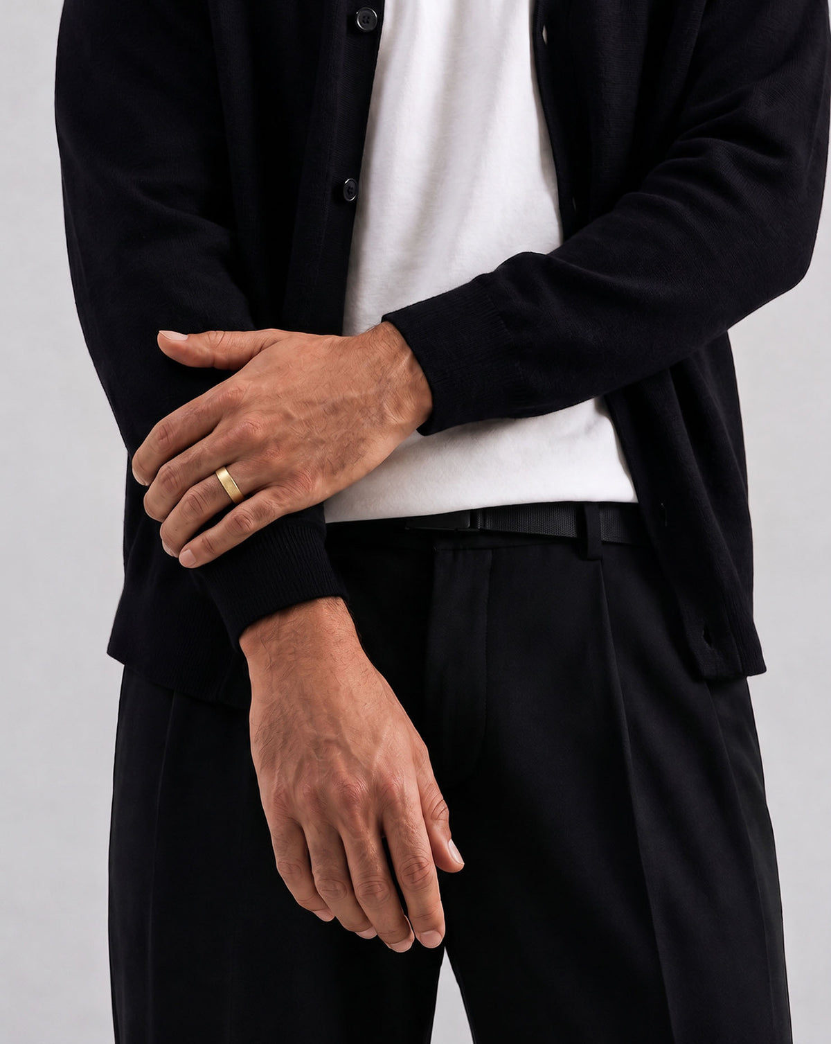 A close-up of a man's hands resting on his lap, wearing a simple gold band ring on his left ring finger.  global