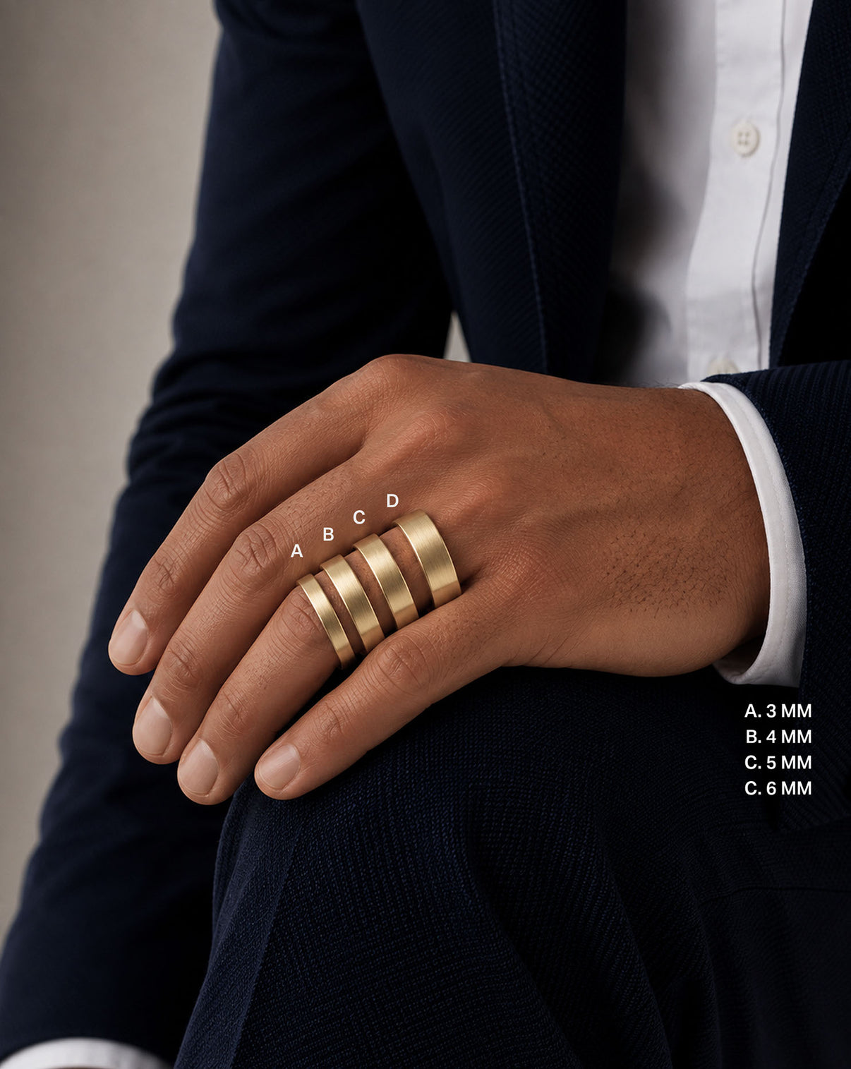 A close-up of a person's hand wearing four wide gold bands rings in varying widths (3mm, 4mm, 5mm, 6mm), styled with a dark navy blazer and white dress shirt. White text overlays indicate the ring widths. global