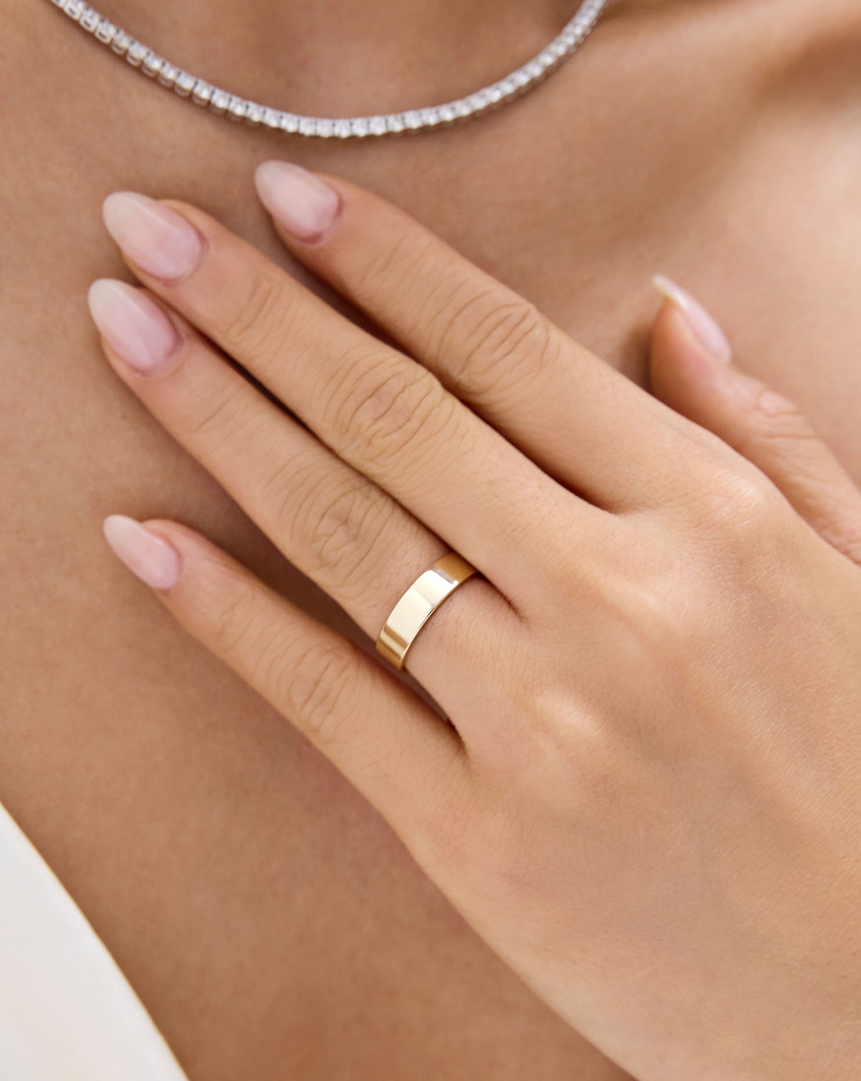 A close-up of a person's hand wearing a simple polished gold band ring global
