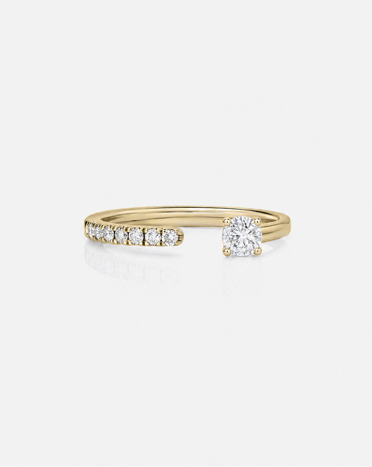 A yellow gold split ring featuring a row of small round-cut diamonds on one side and a larger round-cut diamond on the other, set against a light gray background. 14k yellow gold