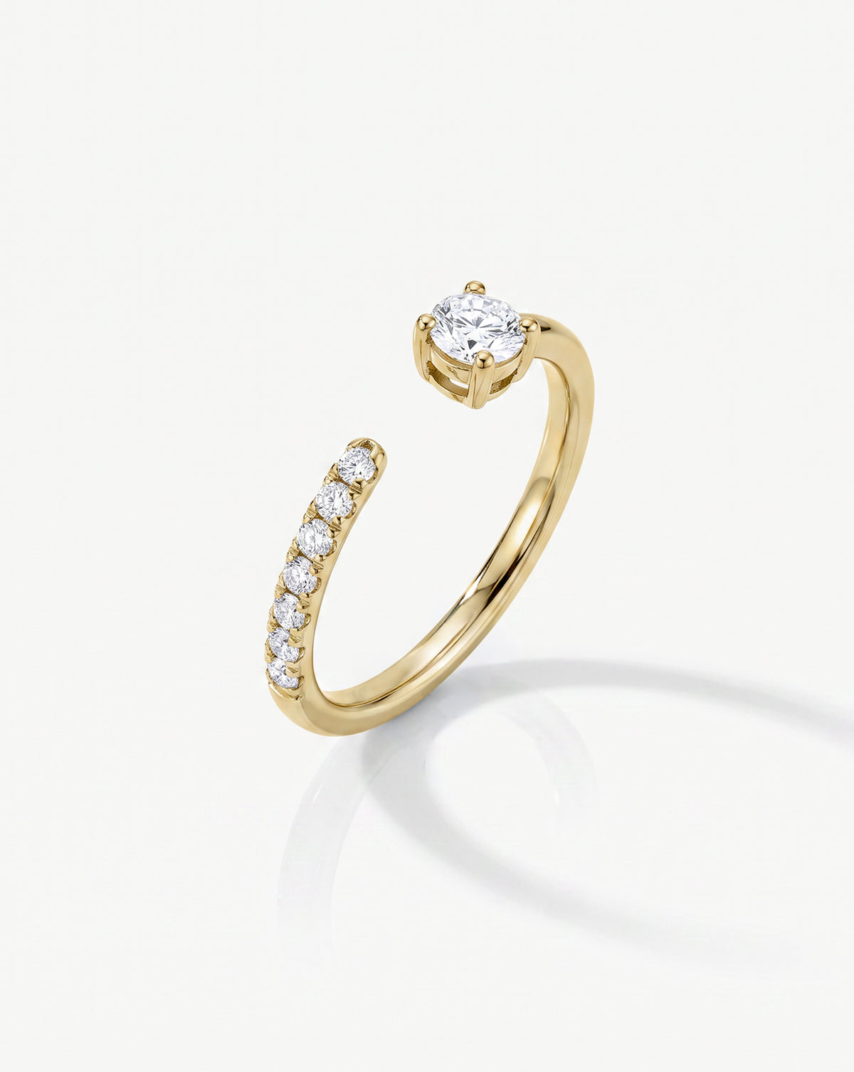 A 14k yellow gold open-band ring featuring a round-cut diamond in a prong setting and a curved row of small diamonds along one side, shown on a clean white background.