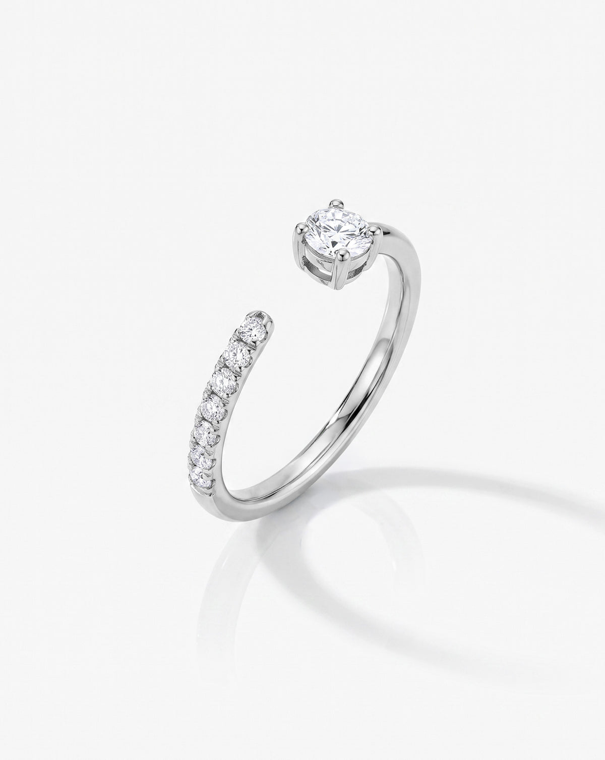 A 14k white gold platinum open band ring featuring a row of small round-cut diamondson one side and a larger center stone on the other, shown on a light gray background side view