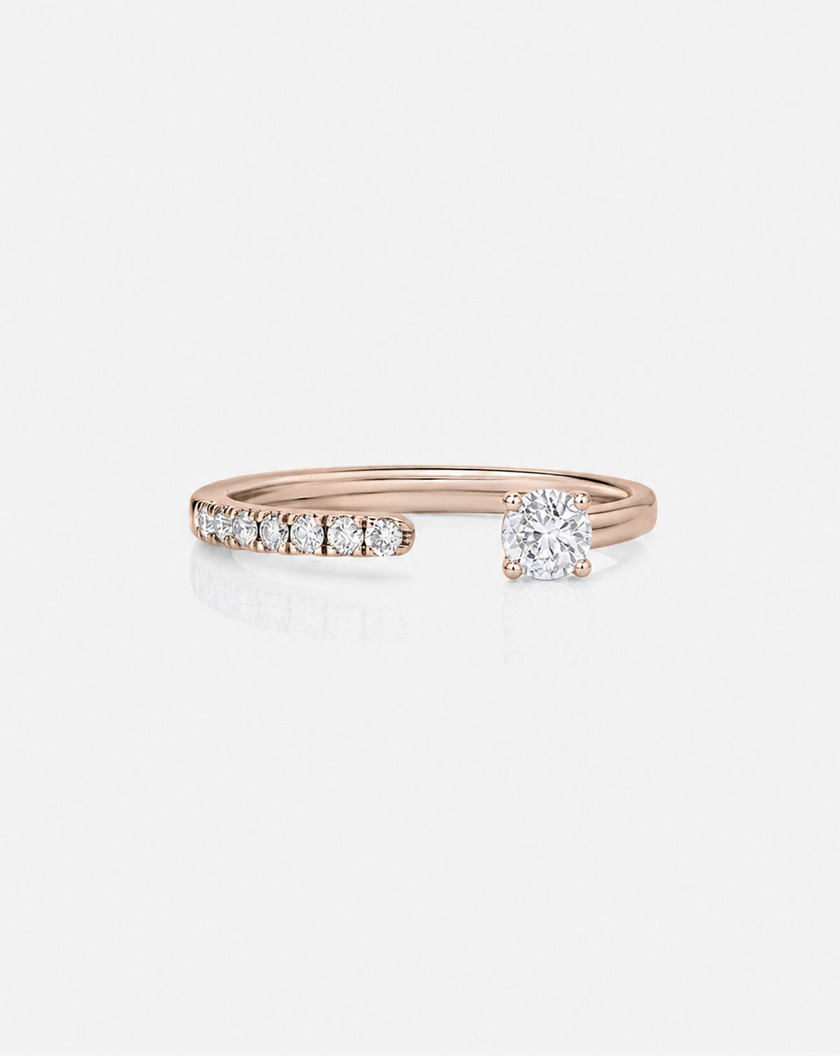 A 14k rose gold open band ring featuring a row of small round-cut diamondson one side and a larger center stone on the other, shown on a light gray background.
