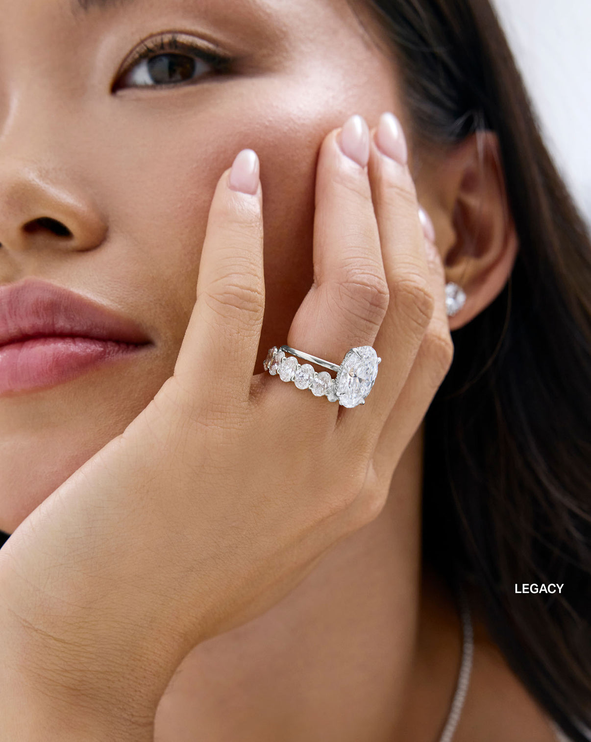 A close-up lifestyle shot of a woman wearing an oval eternity Legacy band with an oval engagement ring global