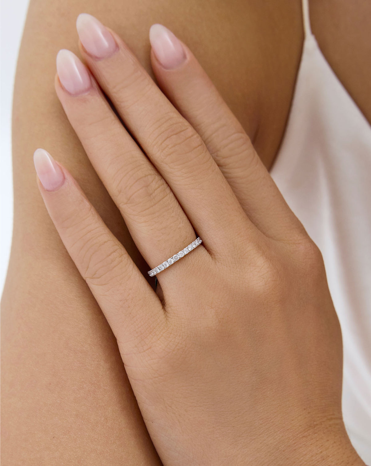 A close-up of a hand with pale pink manicured nails wearing a perfect pave eternity band 1.9 global