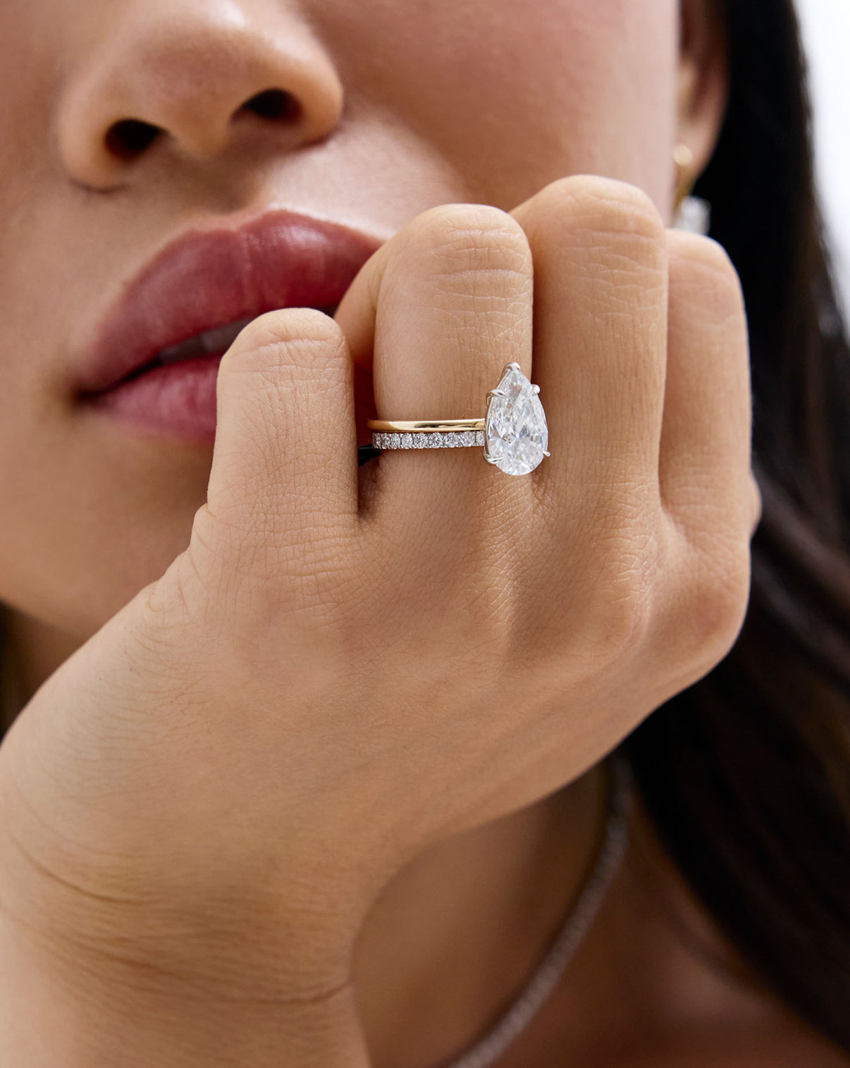 A close-up lifestyle shot of a woman wearing a silver ring with a large pear-engagement ring with perfect pave band global