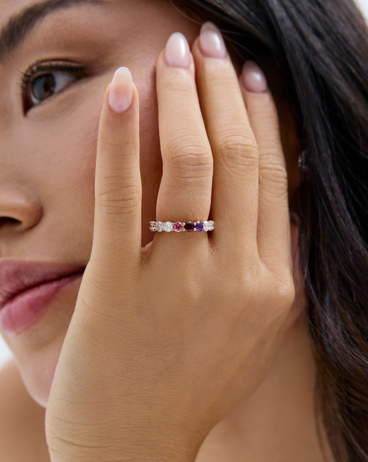 close up of model's face and hand showing the round diamond and birthstone eternity band
global
