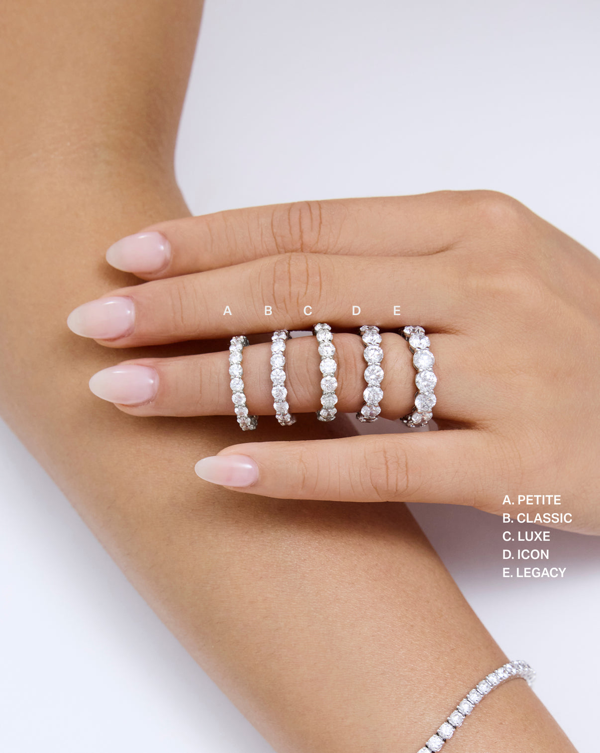 A close-up of a hand wearing five diamond eternity rings in different widths global