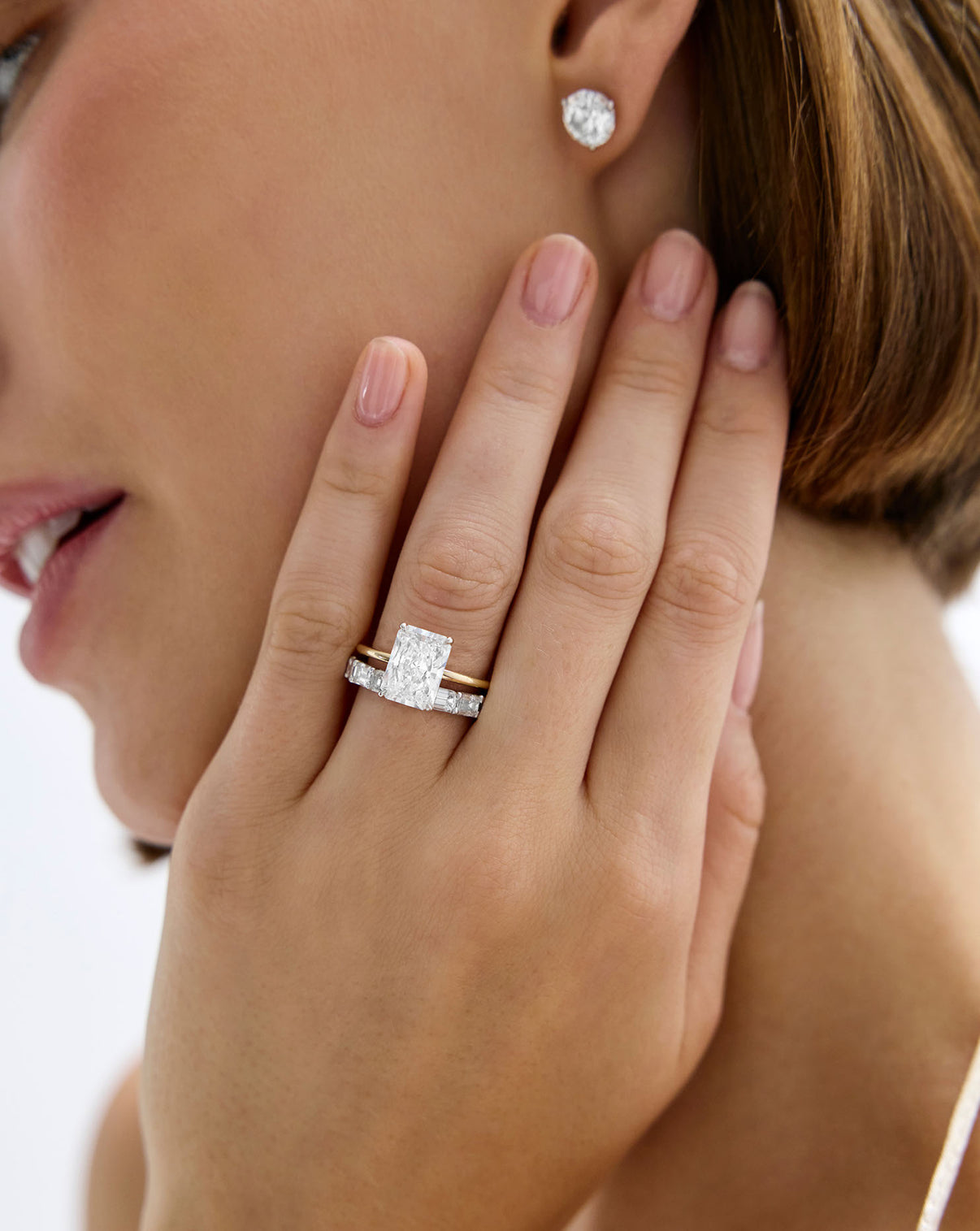Close-up of a hand wearing a Diamond Sideways Emerald Eternity Band with a radiant engagement ring global