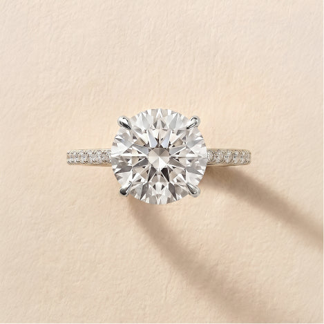 yellow gold round diamond engagement ring with pave band against a neutral textured background