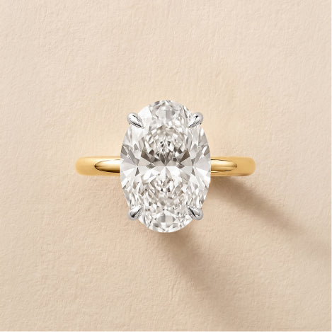 yellow gold oval solitaire diamond whisper thin engagement ring against a neutral textured background