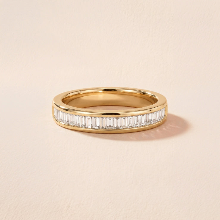 yellow gold baguette channel set diamond eternity wedding band against a textured neutral background
