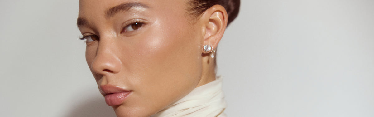 video of a woman wearing a white suit next to a lake, with several layered diamond tennis bracelets and necklaces