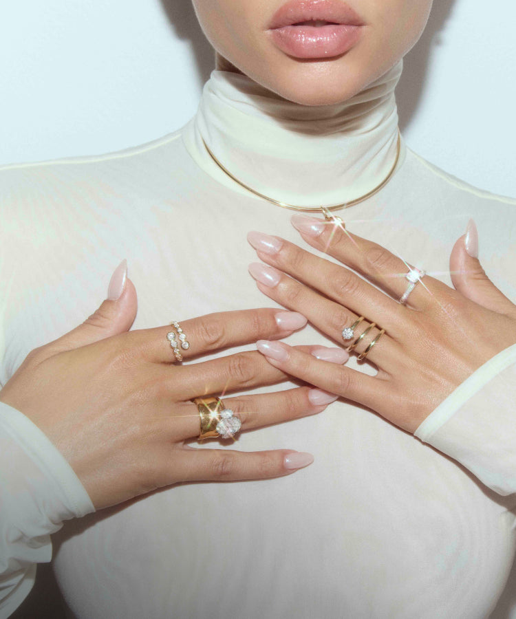 video of a woman wearing a white suit next to a lake, with several layered diamond tennis bracelets and necklaces