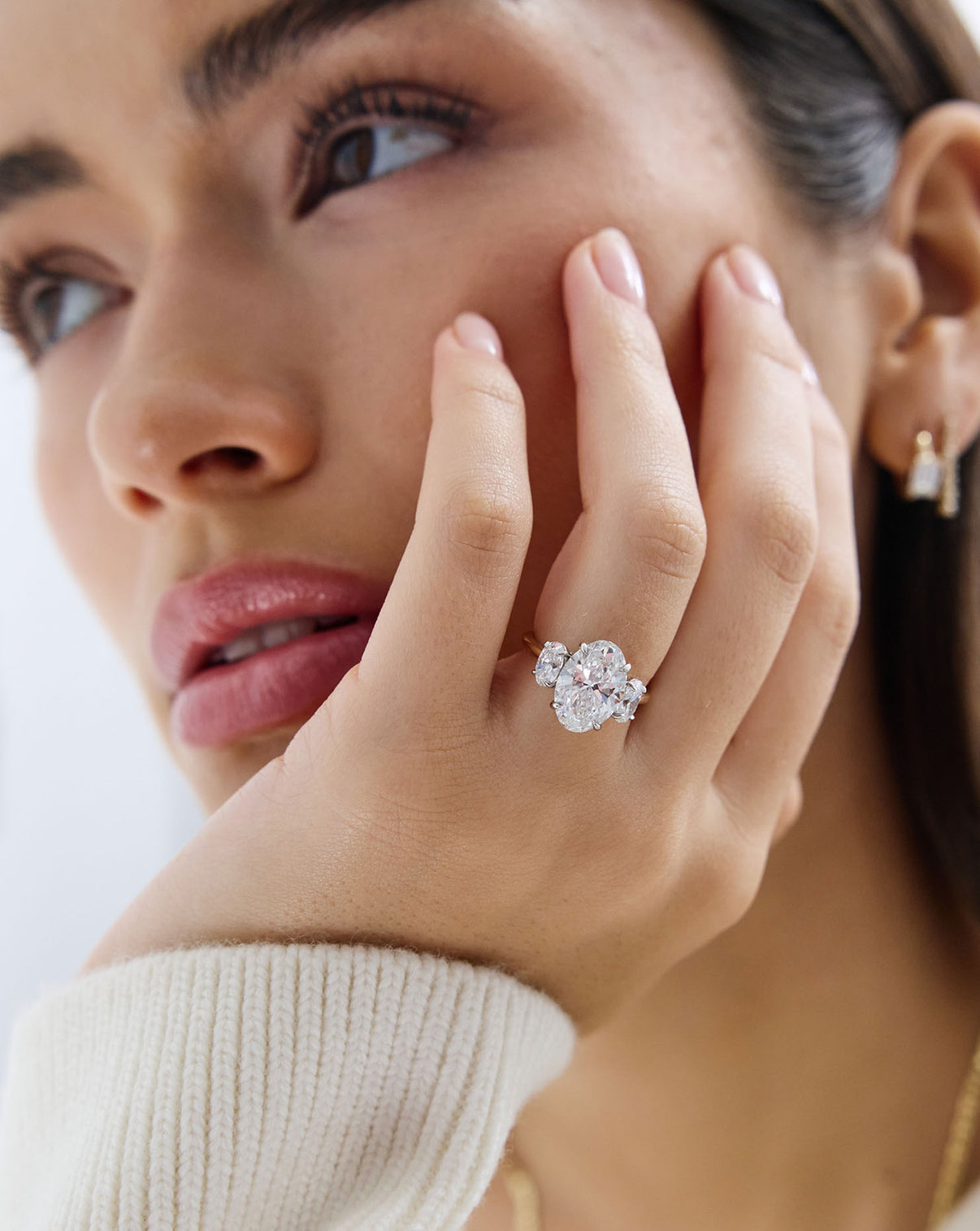 close up of model's hand on her face and wearing a 4 carat Oval Engagement Ring in 14k yellow gold Whisper Thin Three Stone with platinum prongs
