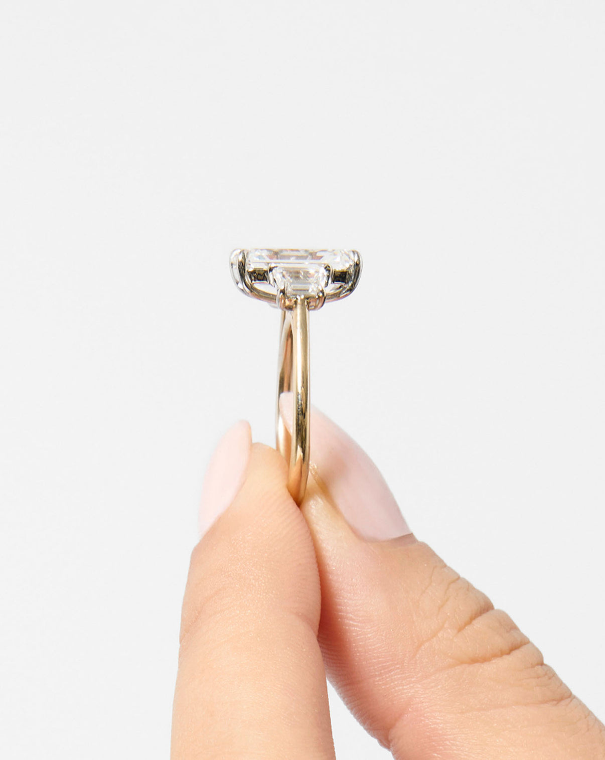 model holding 5 carat Emerald in Yellow Gold Whisper Thin with trapezoid side stones