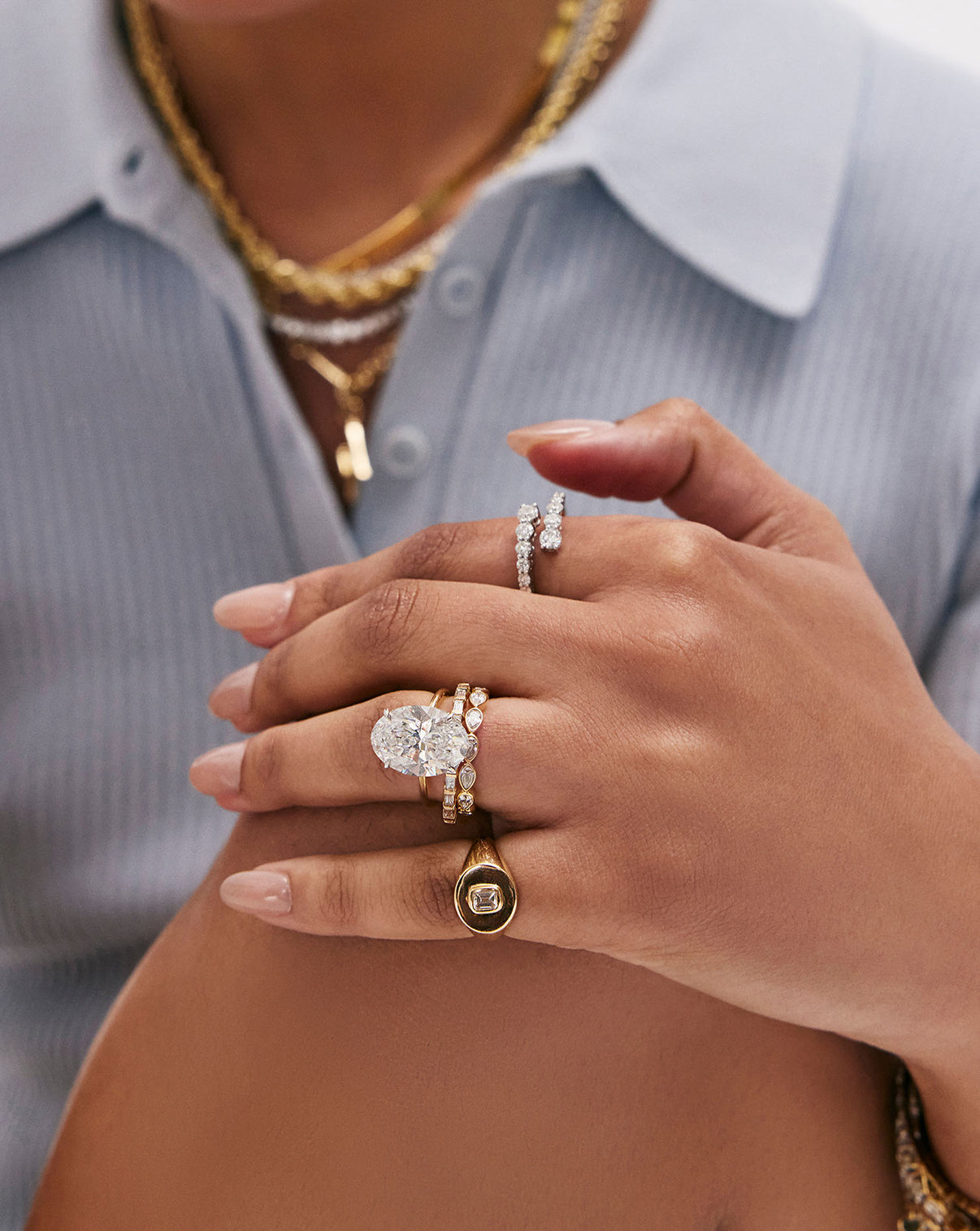 6 carat Oval Diamond Engagement Ring in Yellow Gold Whisper Thin Hidden Halo band with Platinum Prongs styled on model's hand along with various gold and diamond rings