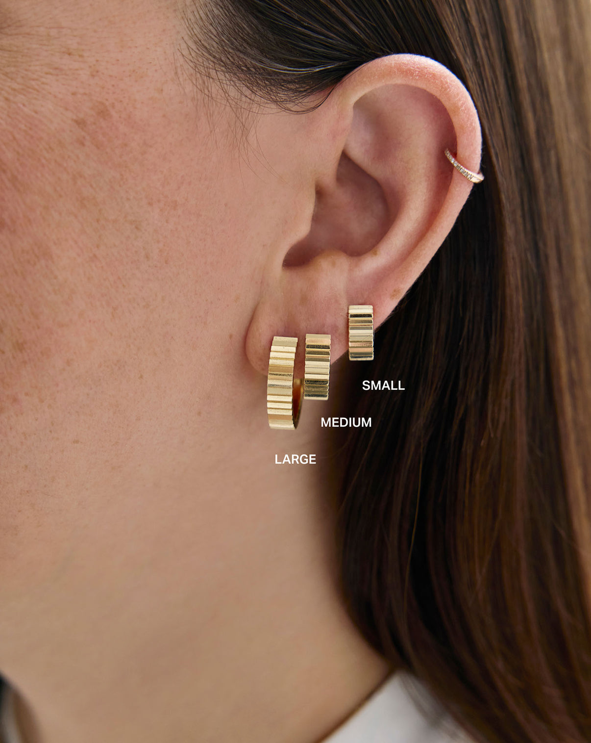 Wide Fluted Gold Hoops large, medium, and small styled with an ear cuff on model. global