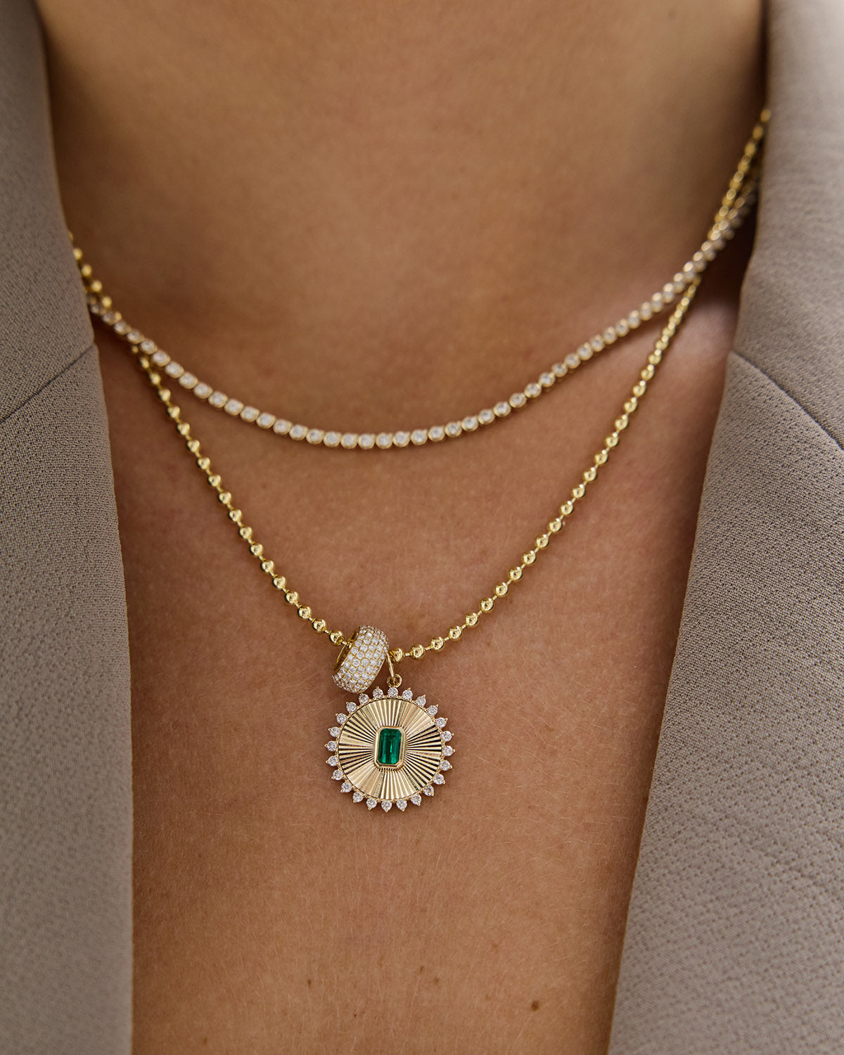 Gold necklace with a pendant featuring an emerald stone on a person's neck.
