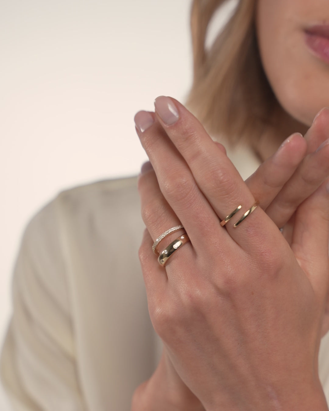 Video of the Open Gold Wrap Ring in Yellow Gold on the pointer finger hand stacked with the Double Row Stackable Pavé Ring and Luxe Inlay Eternity Band in Yellow Gold holding other hand in front of model's face GLOBAL