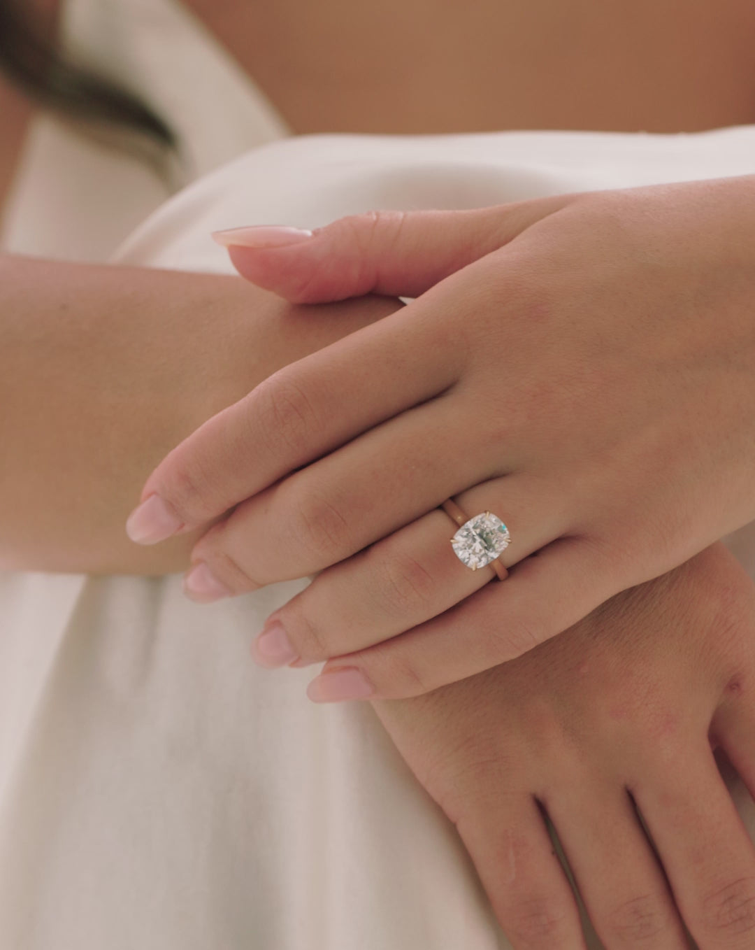 Video of model wearing 4.05 carat cushion cut lab-grown diamond engagement ring with cathedral-style yellow gold band, arms crossed close-up