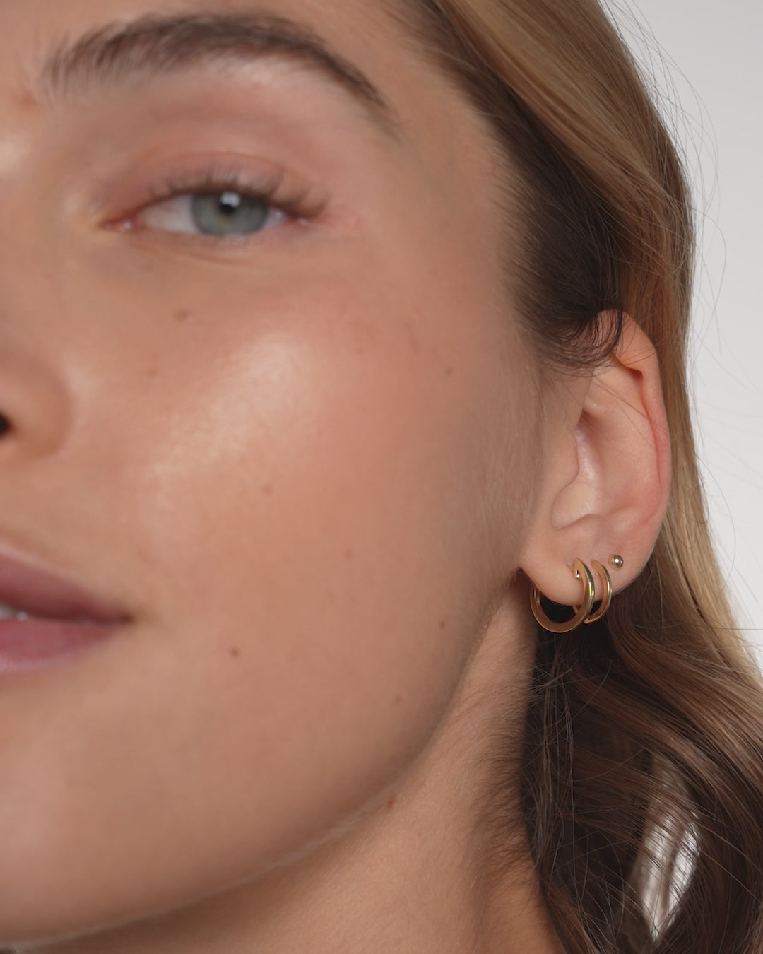 Video of Classic Gold Huggies in 14k Yellow Gold styled on model's ear stacked with other huggie and stud styles 
