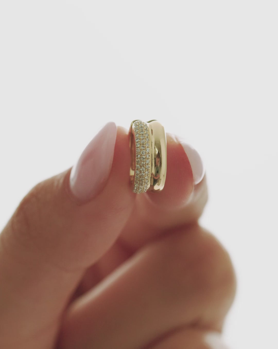 Close-up video of a gold double-row pavé ear cuff with sparkling clear stones held between fingers against a white background.